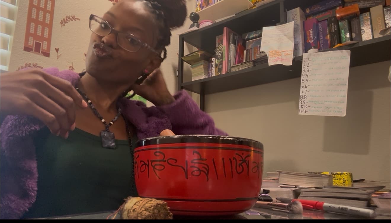 Woman in purple robe posing behind a large red singing bowl with black script.