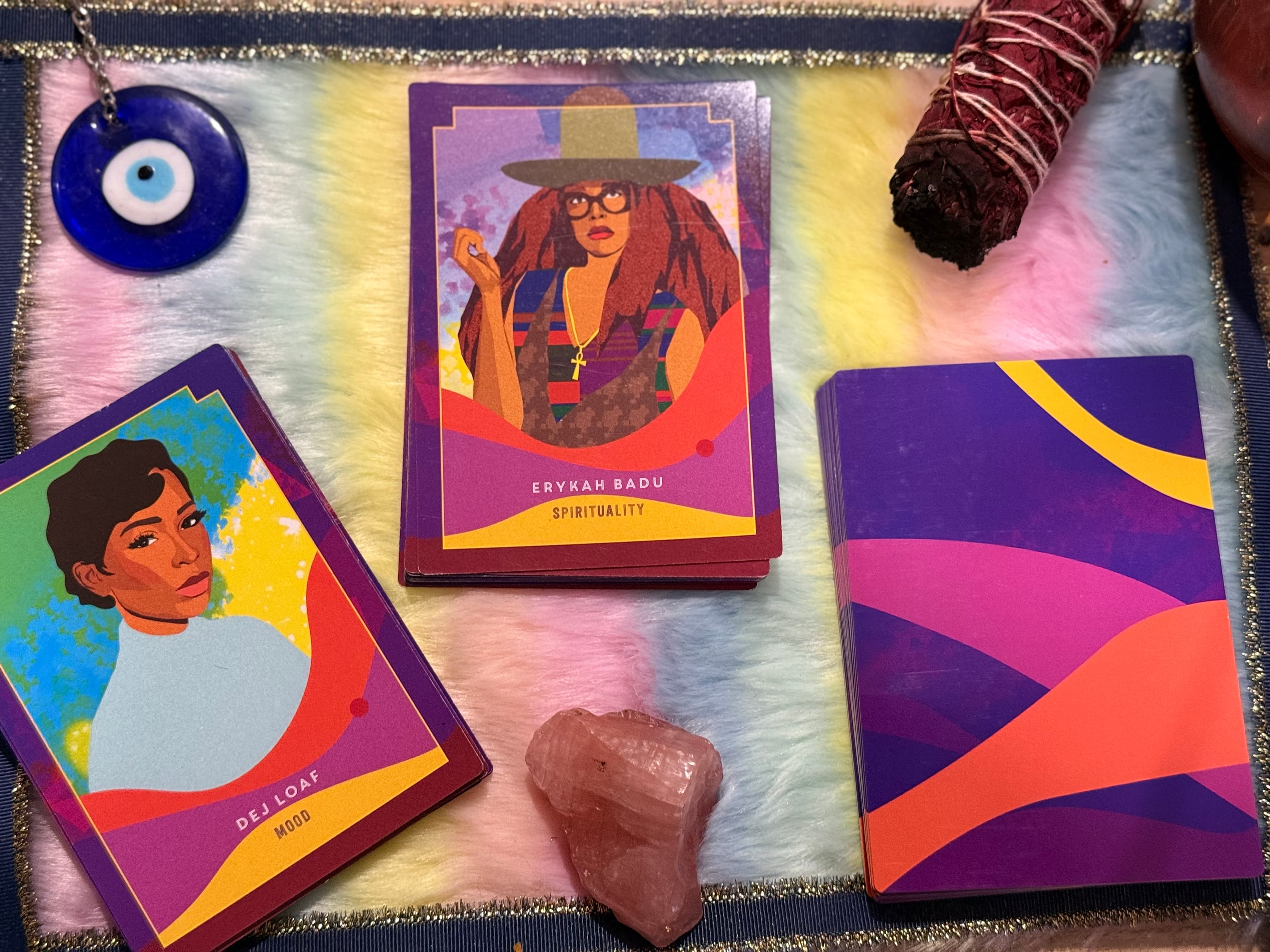 Oracle cards featuring Erykah Badu and Dej Loaf with rose quartz, sage, and evil eye.