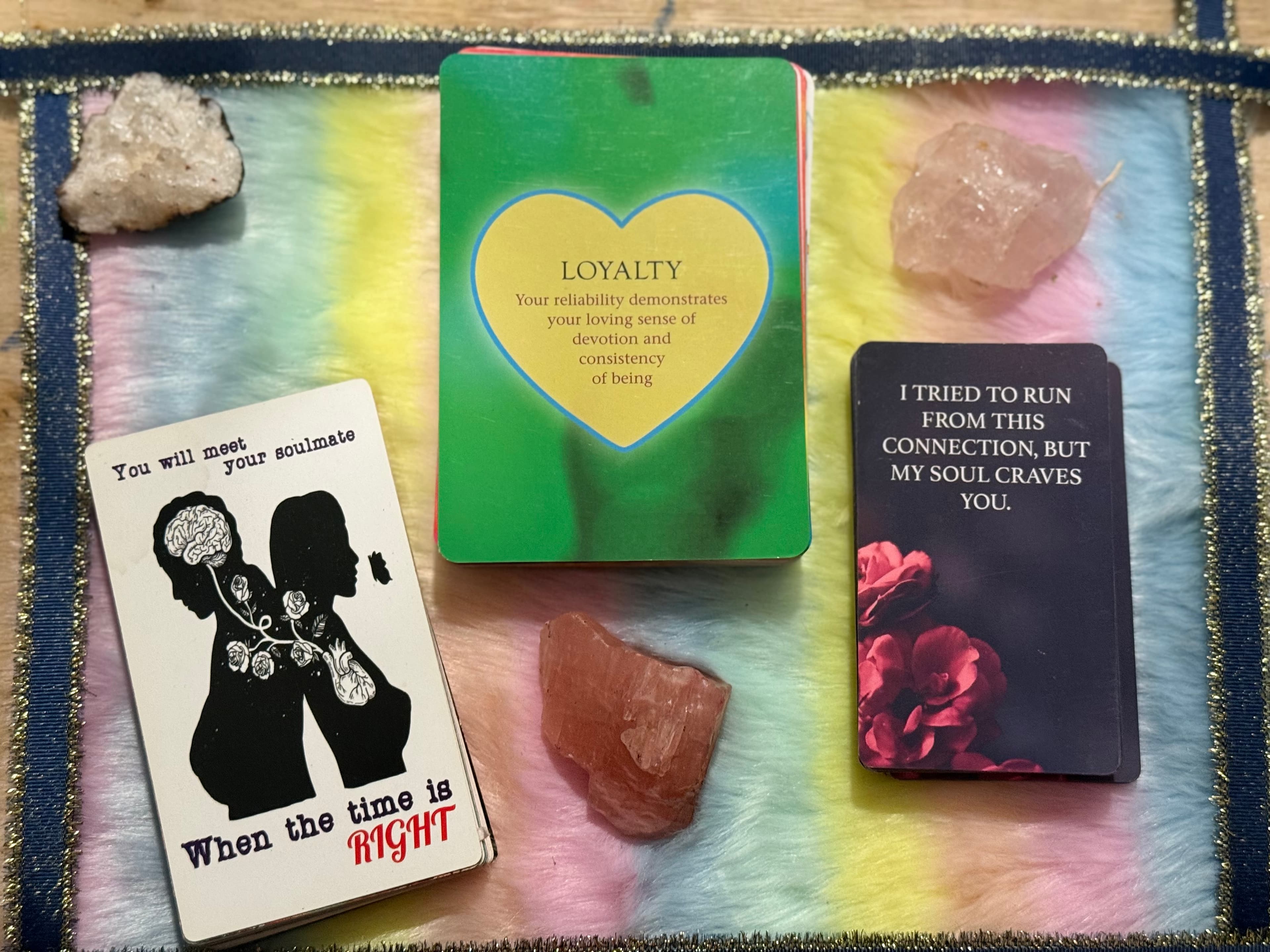 Three oracle cards and crystals on a rainbow mat featuring messages about soulmates and loyalty.