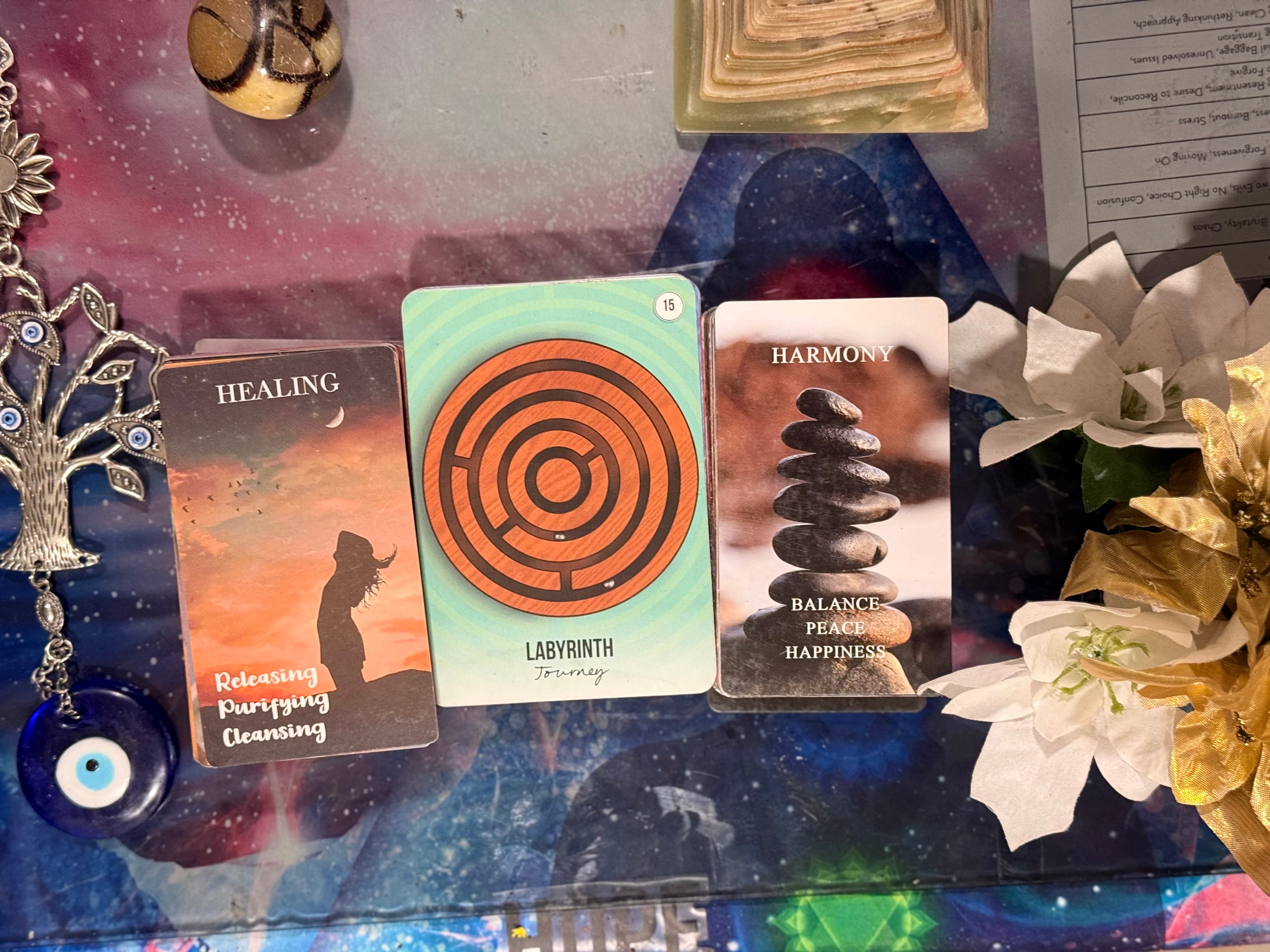 Three oracle cards titled Healing, Labyrinth, and Harmony surrounded by spiritual charms and flowers.