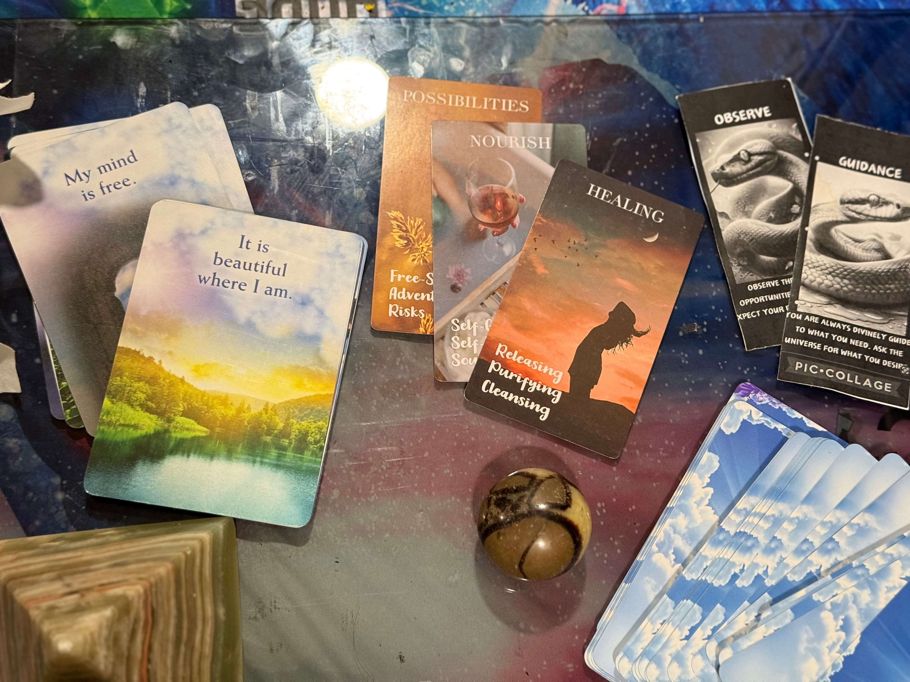 Inspirational affirmation cards, a patterned stone, and a small pyramid on a reflective surface.